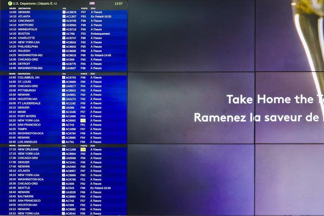 Airport Departure Board With Take Home the Taste Advertisement - A close-up shot of an airport departure board showing various flight times and destinations with an advertisement for Take Home the Taste with a French translation below it. The advertisement is partially